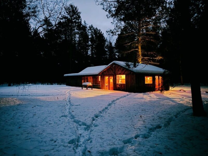 Vinterklädd trästuga med upplysta fönster i en snötäckt skog